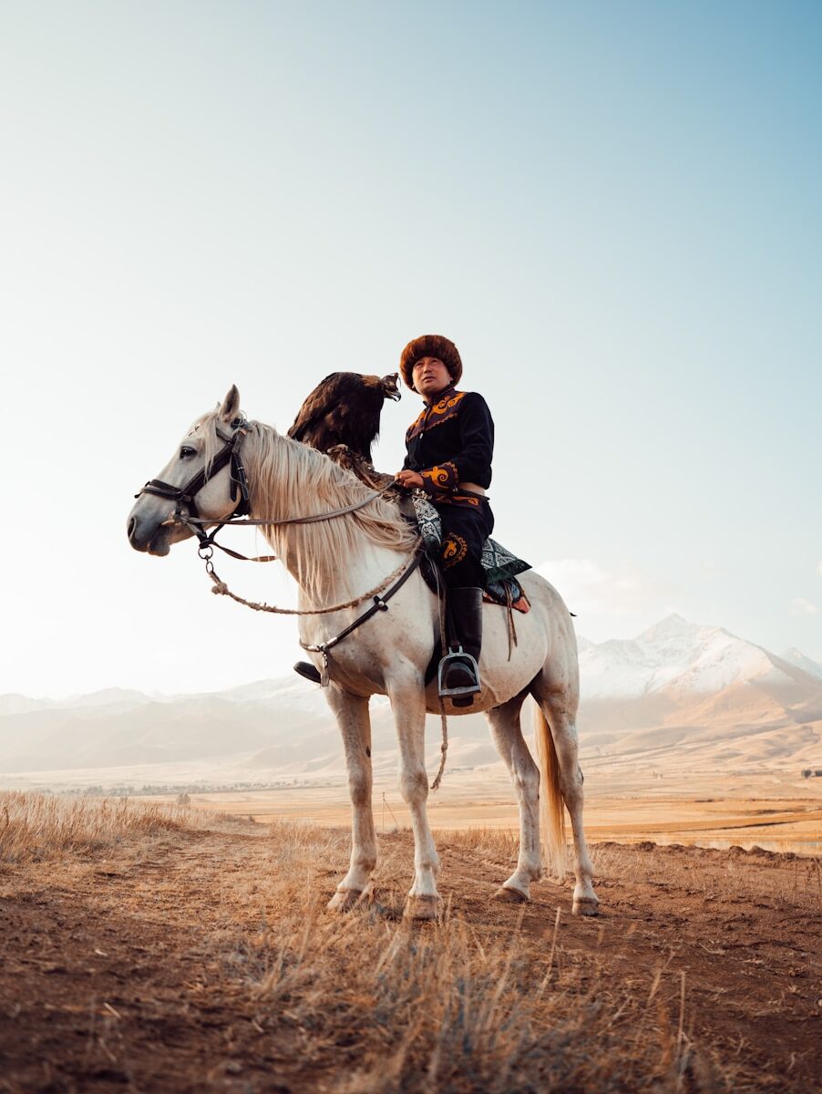 Person in traditional clothing riding white horse with eagle.